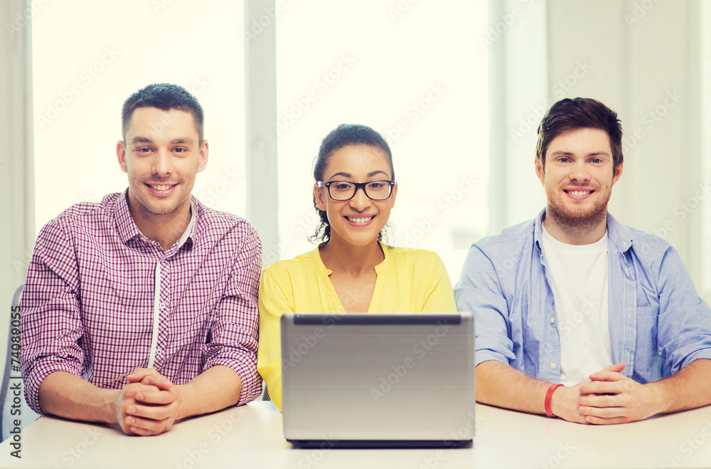 three smiling colleagues with laptop in office three smiling colleagues with laptop in office