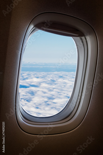 Quadro em tela Plane window with blue sky and clouds outside.