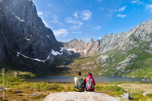 Young tourist couple sitting on stone near mountain lake