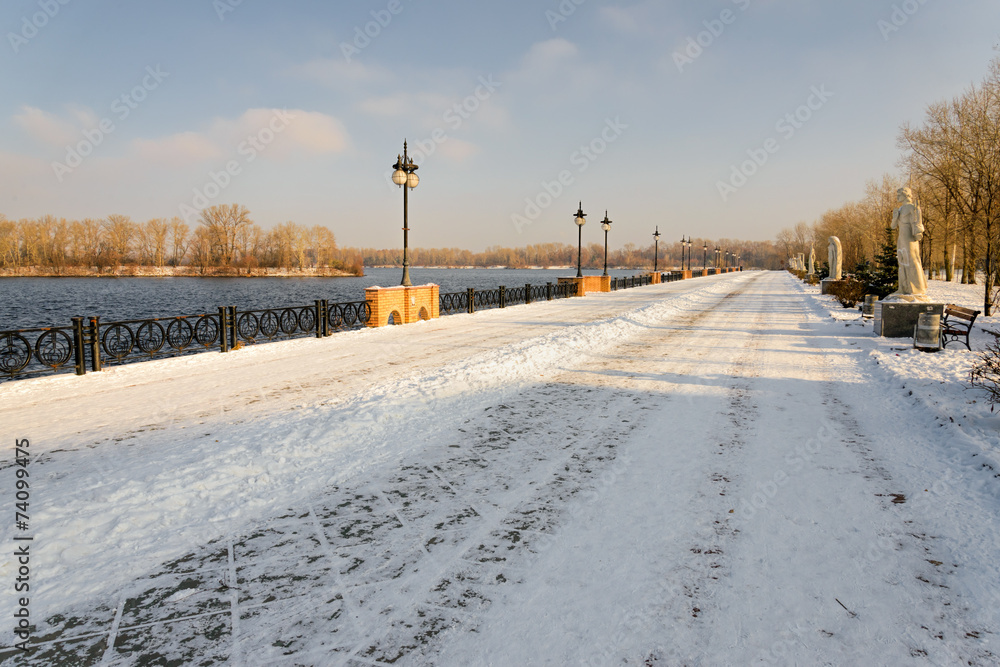 Late afternoon promenade in the park, close to the Dnieper river, in winter. The soil is covered by cold snow and ice