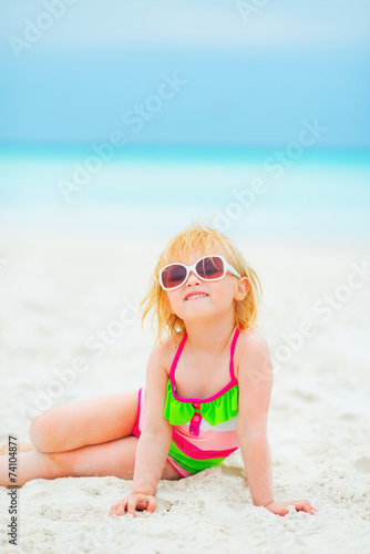 Portrait of happy baby girl in sunglasses sitting on beach