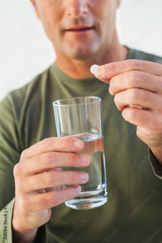Mid section of a man holding glass of water and pill Mid section of a man holding glass of water and pill