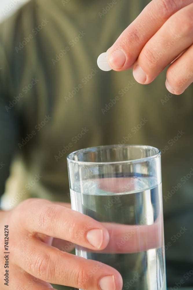 Close up of a man holding glass of water and pill