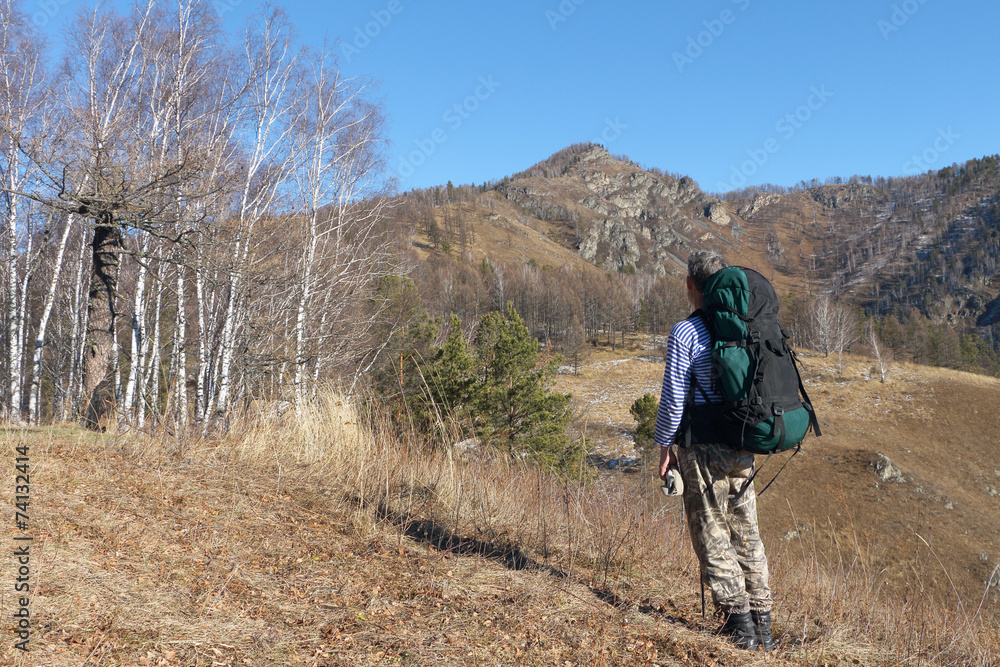 The tourist with a backpack standing at the foot of the mountain
