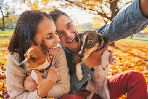 Canvas Print Smiling young couple with dogs outdoors in autumn park