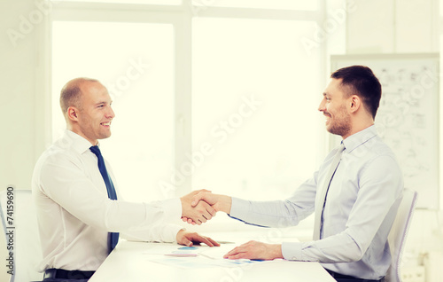 two smiling businessmen shaking hands in office