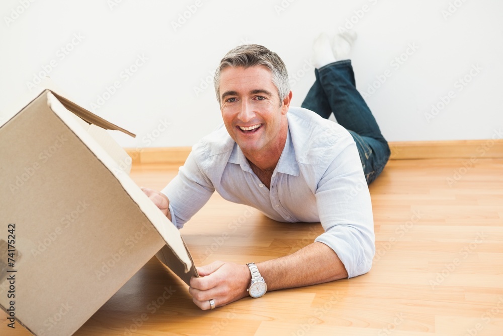 Happy man lying on floor with box looking at camera Happy man lying on floor with box looking at camera