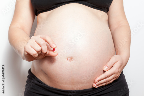 Closeup of pregnant woman holding pills, isolated on white
