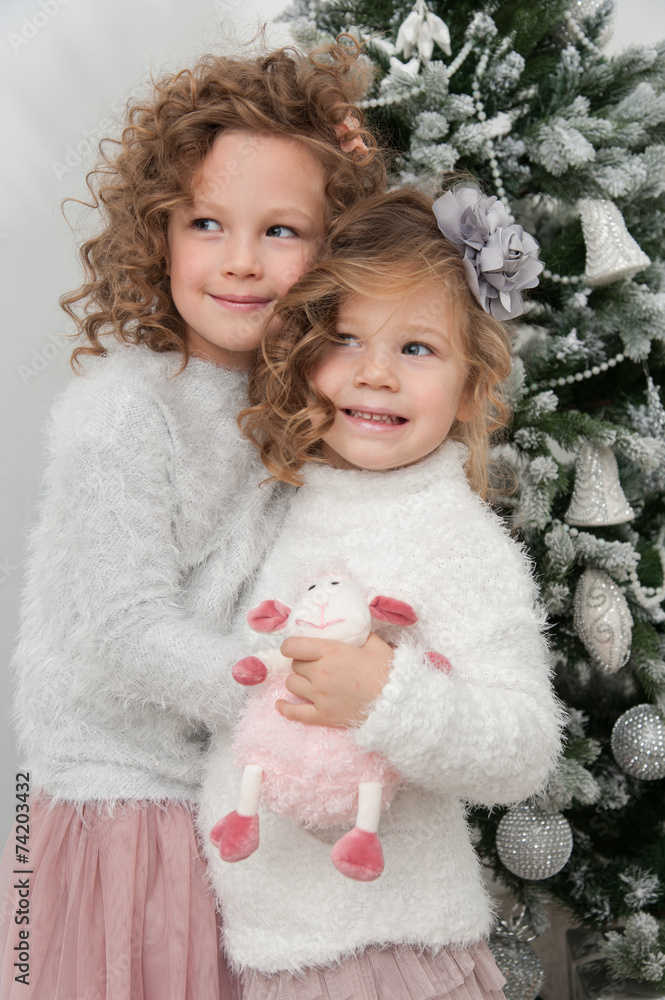 Cute child girls with sheep toy stand near Christmas tree Cute child girls with sheep toy stand near Christmas tree