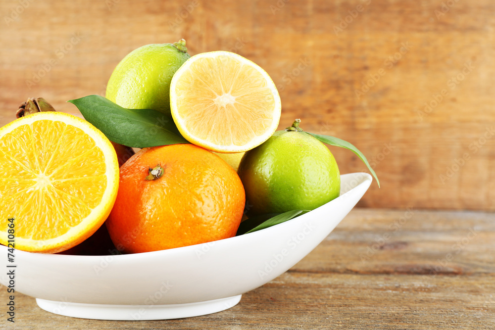 Ripe citrus with green leaves on plate on wooden background Ripe citrus with green leaves on plate on wooden background