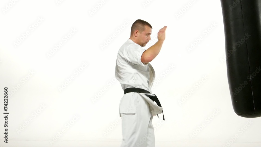 Black belt karate man practicing on the sandbag on white Black belt karate man practicing on the sandbag on white