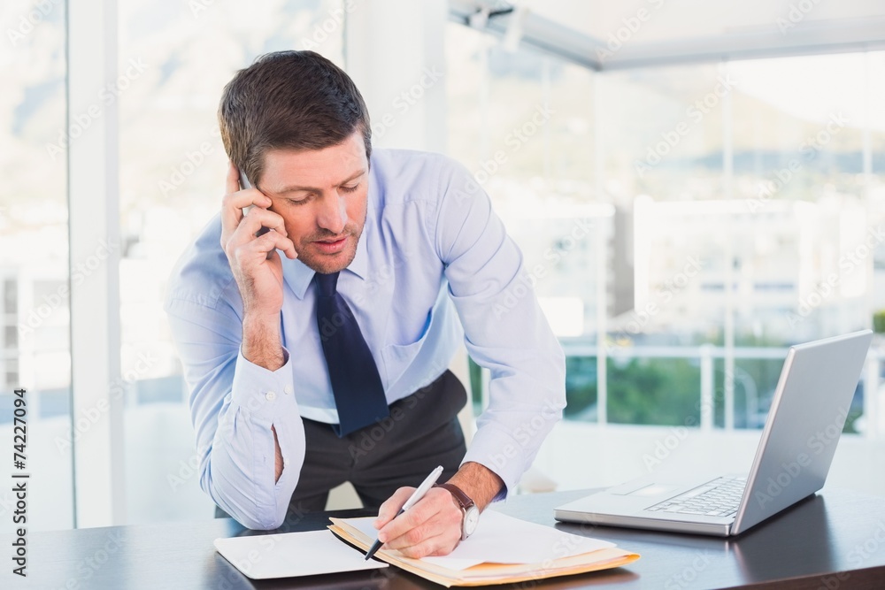 Businessman writing and phoning at his desk Businessman writing and phoning at his desk