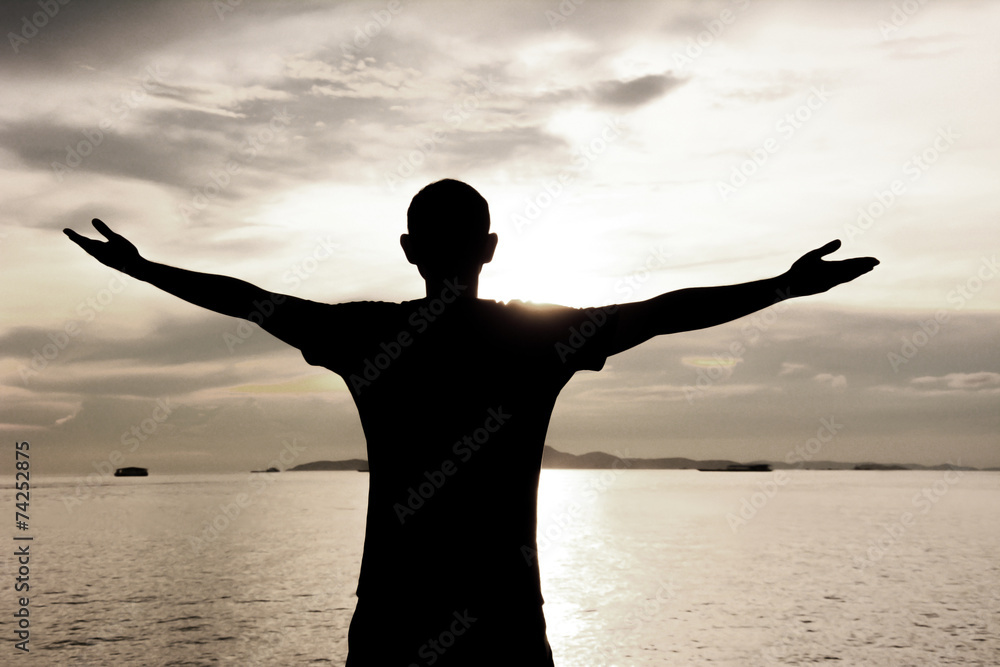 Silhouette of a man raising his arms on twilight sky background