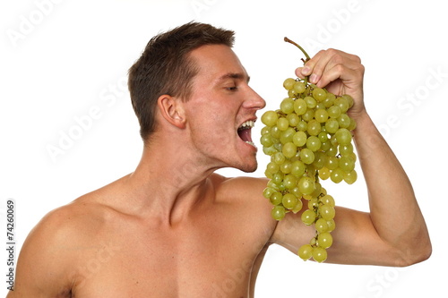 Athletic young man shirtless eats grapes on white background