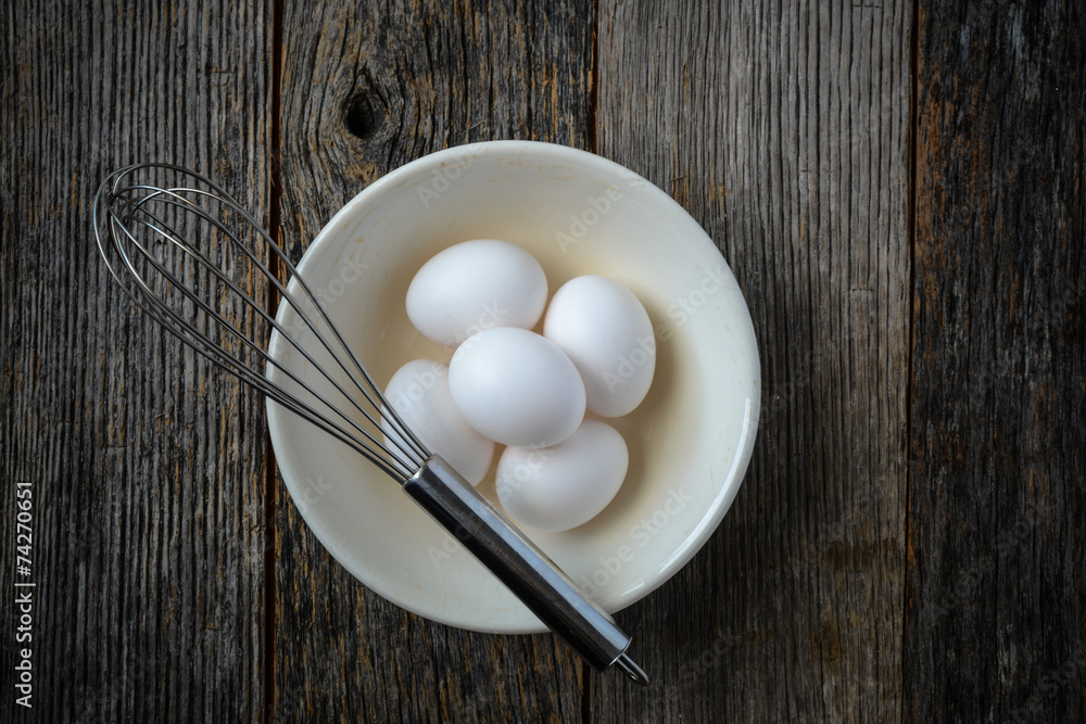 Eggs in a Bowl with a Whisk on Rustic Wood Background Eggs in a Bowl with a Whisk on Rustic Wood Background