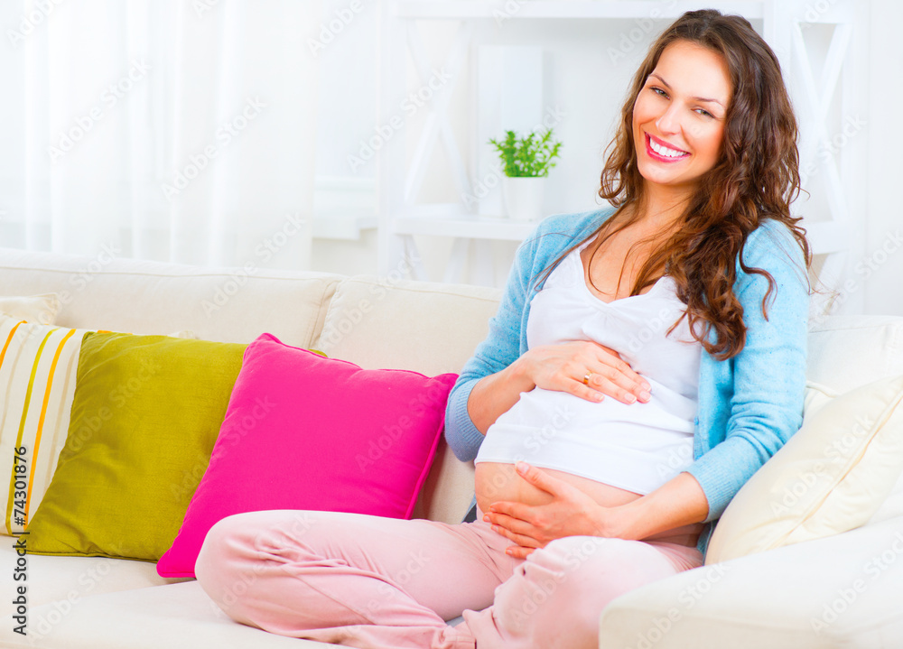 Pregnant woman sitting on a sofa and caressing her belly Pregnant woman sitting on a sofa and caressing her belly