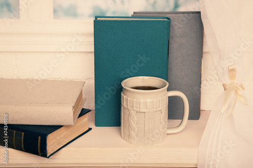 Old books and cup of coffee on windowsill