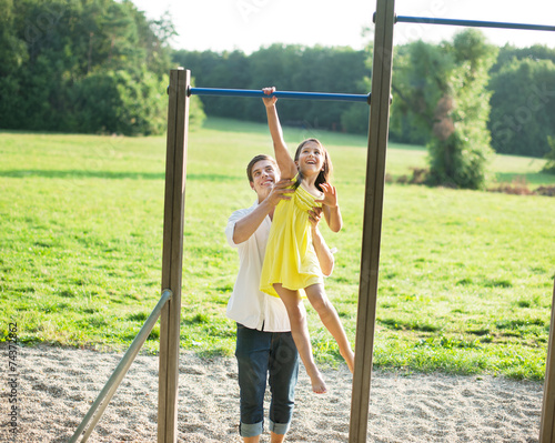 Junger Vater hilft Tochter auf dem Spielplatz photo