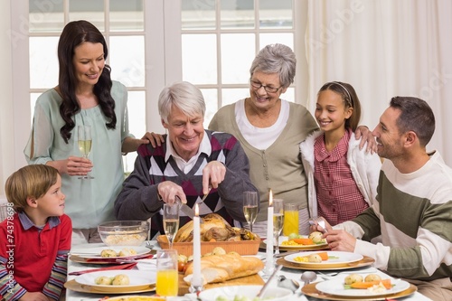 Grandfather carving chicken and his family looking him