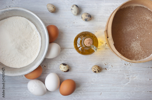 Eggs, flour and a bottle of olive oil on the white wooden table