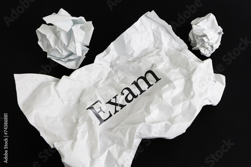 Crumpled paper sheet with word Exam isolated on black