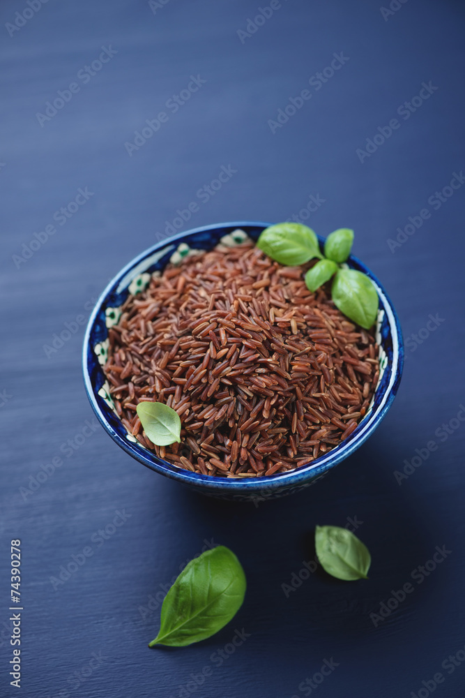 Red kernel rice in a ceramic pialat, dark blue wooden surface Red kernel rice in a ceramic pialat, dark blue wooden surface