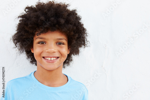 Smiling Young Boy Standing Outdoors Against White Wall