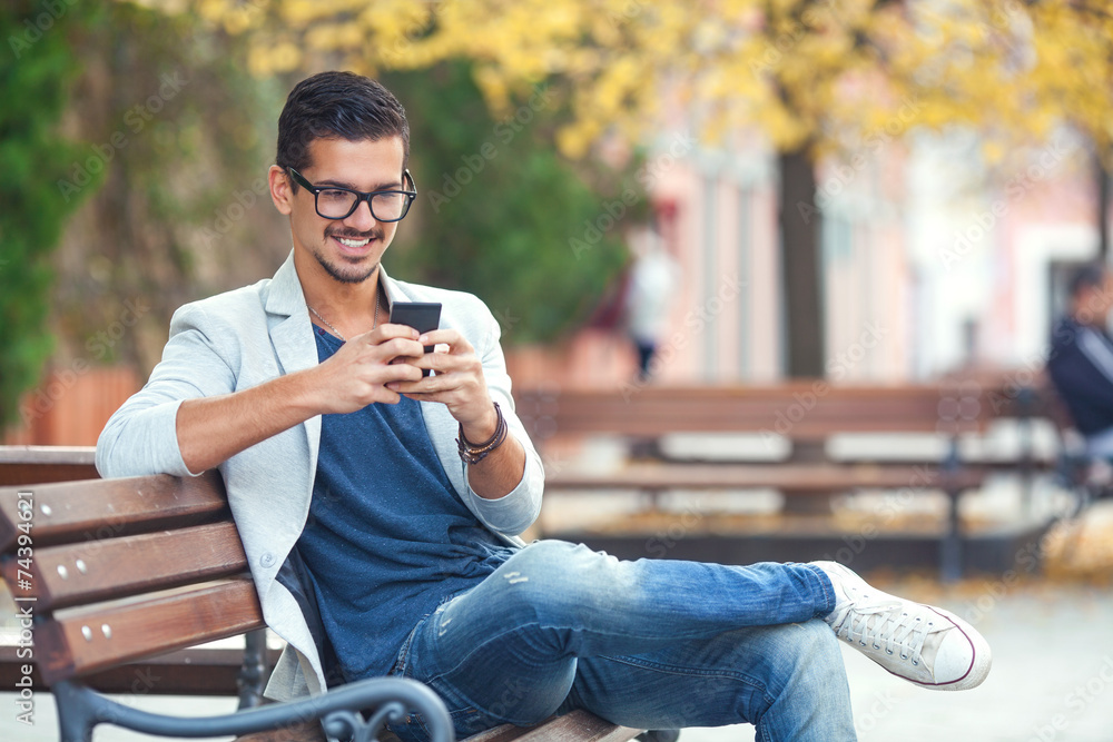 Smiling young man texting on the cellphone Smiling young man texting on the cellphone