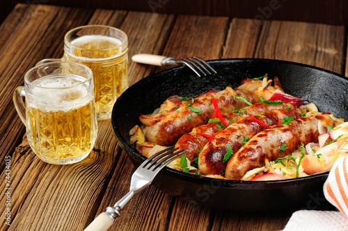 Sausages fried in cast iron skillet with two beer mugs