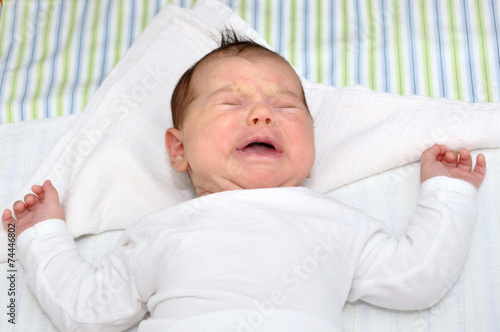 Cute newborn baby girl crying and lying in bed