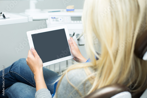 Junge Dame in Zahnarztstuhl schaut auf Tablet