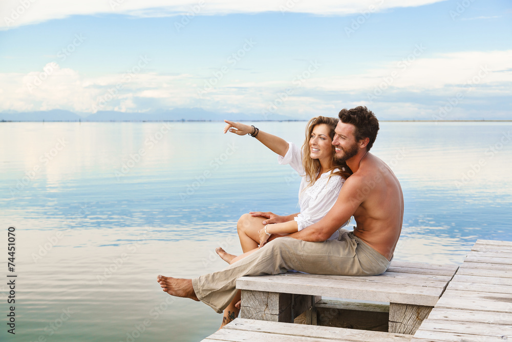 Smiling Couple sitting on a jetty and pointing to the horizon Smiling Couple sitting on a jetty and pointing to the horizon