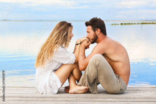 couple sitting on a jetty under a blue sky at a sunset