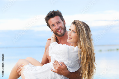 man holding woman in his arms under a blue sky on seaside backgr