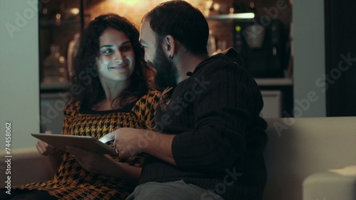 Couple using tablet on sofa at night in room