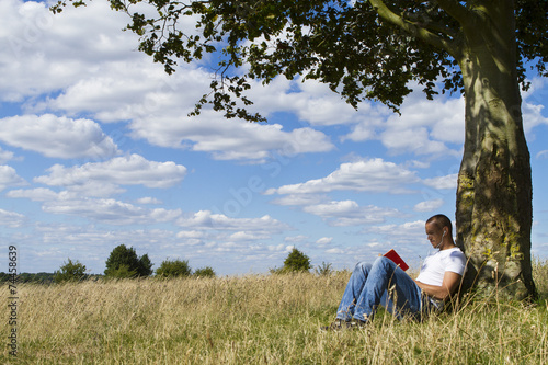 Man reading a book under the shade of a tree