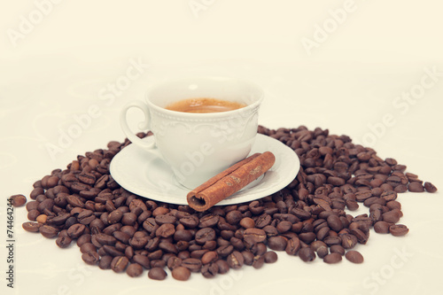 The cup of black coffee with grains and cinnamon stick, toned