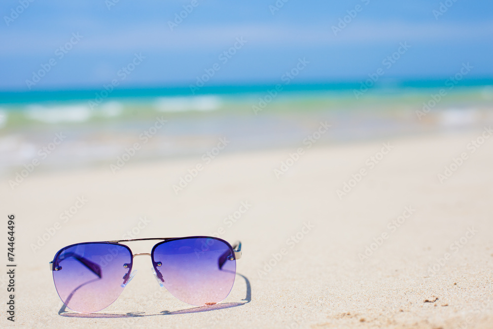blue sunglasses lying on tropical sand beach. party