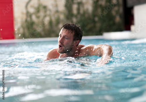 Young wet sexy muscular man posing in the swimming pool 