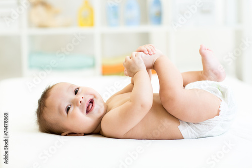 baby lying on white bed and holding legs