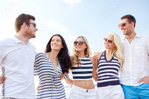 smiling friends in sunglasses talking on beach © Syda Productions