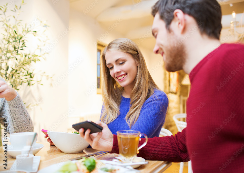 smiling couple with smartphones meeting at cafe