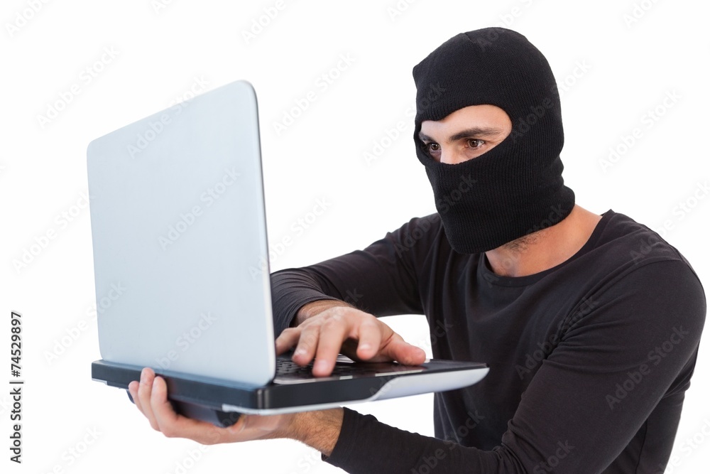 Focused burglar with balaclava holding laptop Focused burglar with balaclava holding laptop