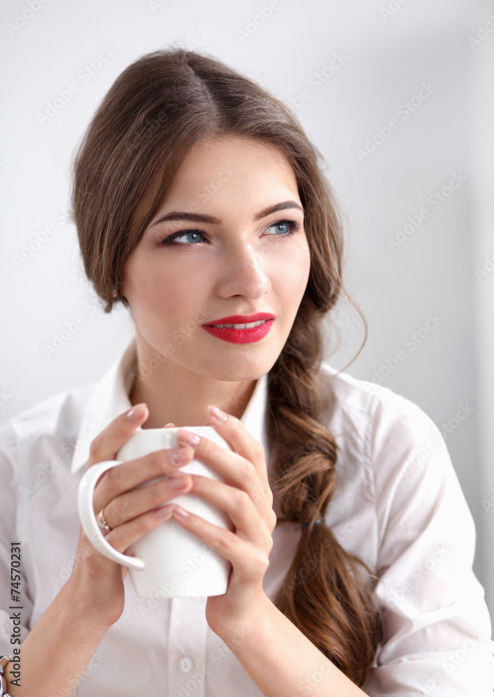 Young businesswoman sitting on the desk with cup in office Young businesswoman sitting on the desk with cup in office