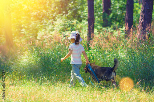 Happy little girl with dog walking in the forest