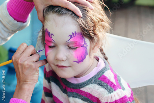 Female hand drawing purple butterfly on face