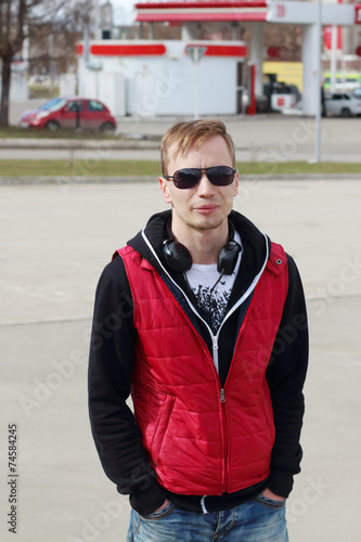 Young man in sunglasses and red vest stands