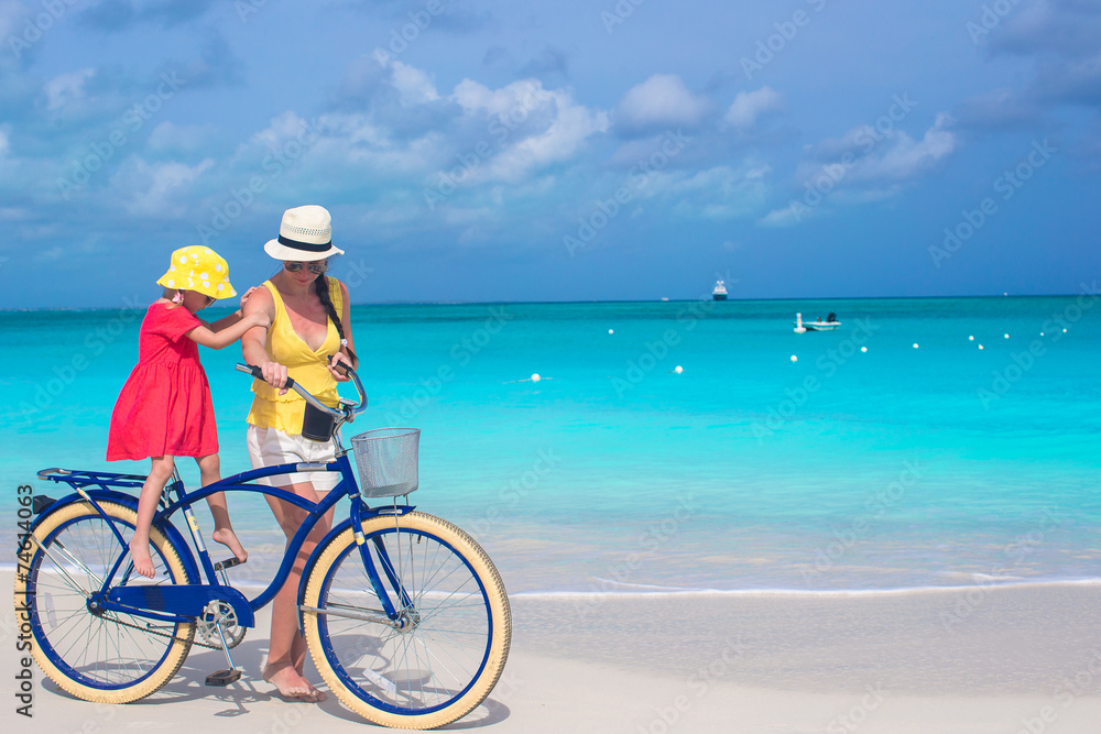 Obraz premium Happy mom and cute girl riding bicycles on tropical beach