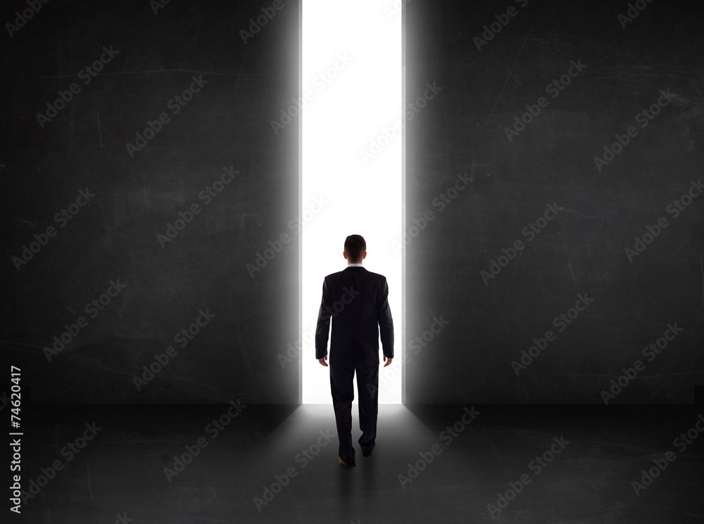 Business person looking at wall with light tunnel opening Business person looking at wall with light tunnel opening