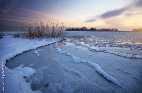 Beautiful winter landscape with frozen lake and sunset sky.